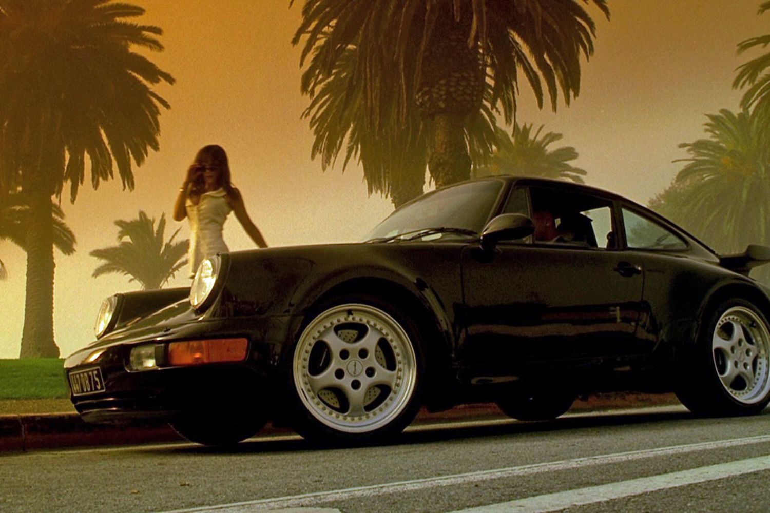 Woman approaches Porsche 993 Turbo on palm-lined road.