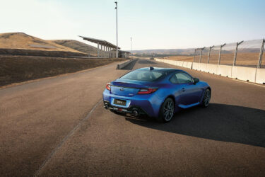 Blue Subaru BRZ on empty track, hills visible.